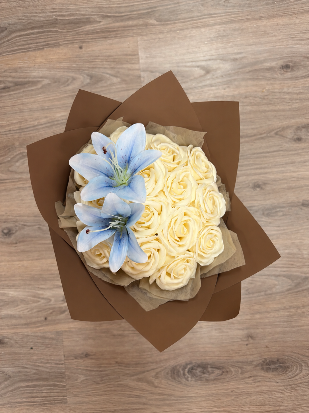 Bouquet Vaea de roses vanille et lys bleu ciel posé sur un parquet, photo réelle