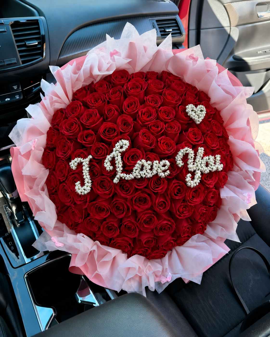 Bouquet Lara de roses rouges avec message I Love You posé sur un siège de voiture