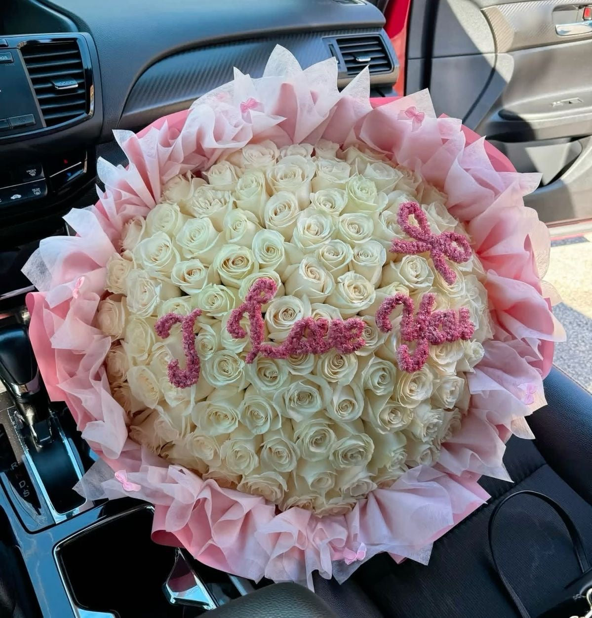 Bouquet Amoureuse de roses blanches avec message I Love You posé sur un siège de voiture