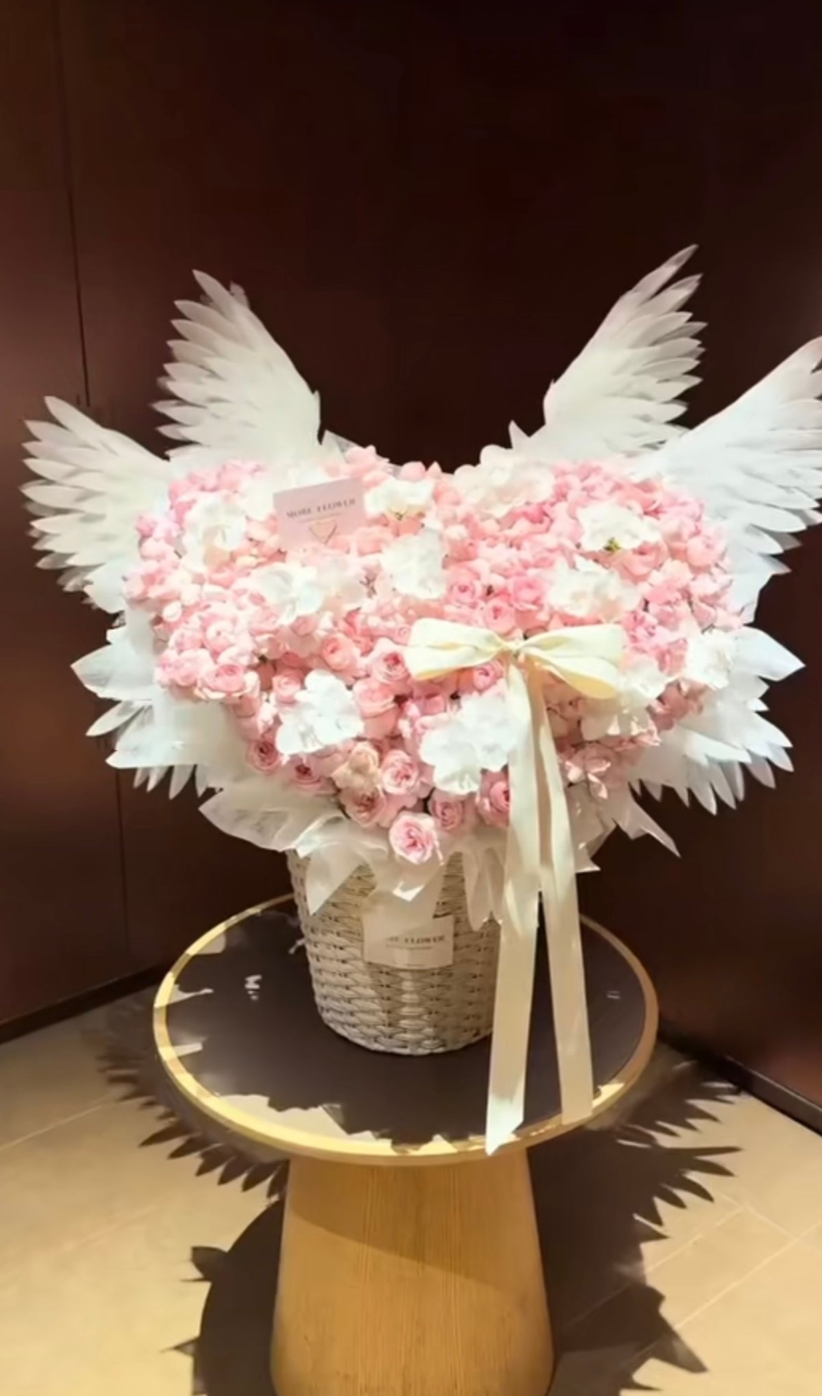 Cœur ANGEL de roses éternelles rose pâle avec ailes blanches et ruban, présenté sur un guéridon