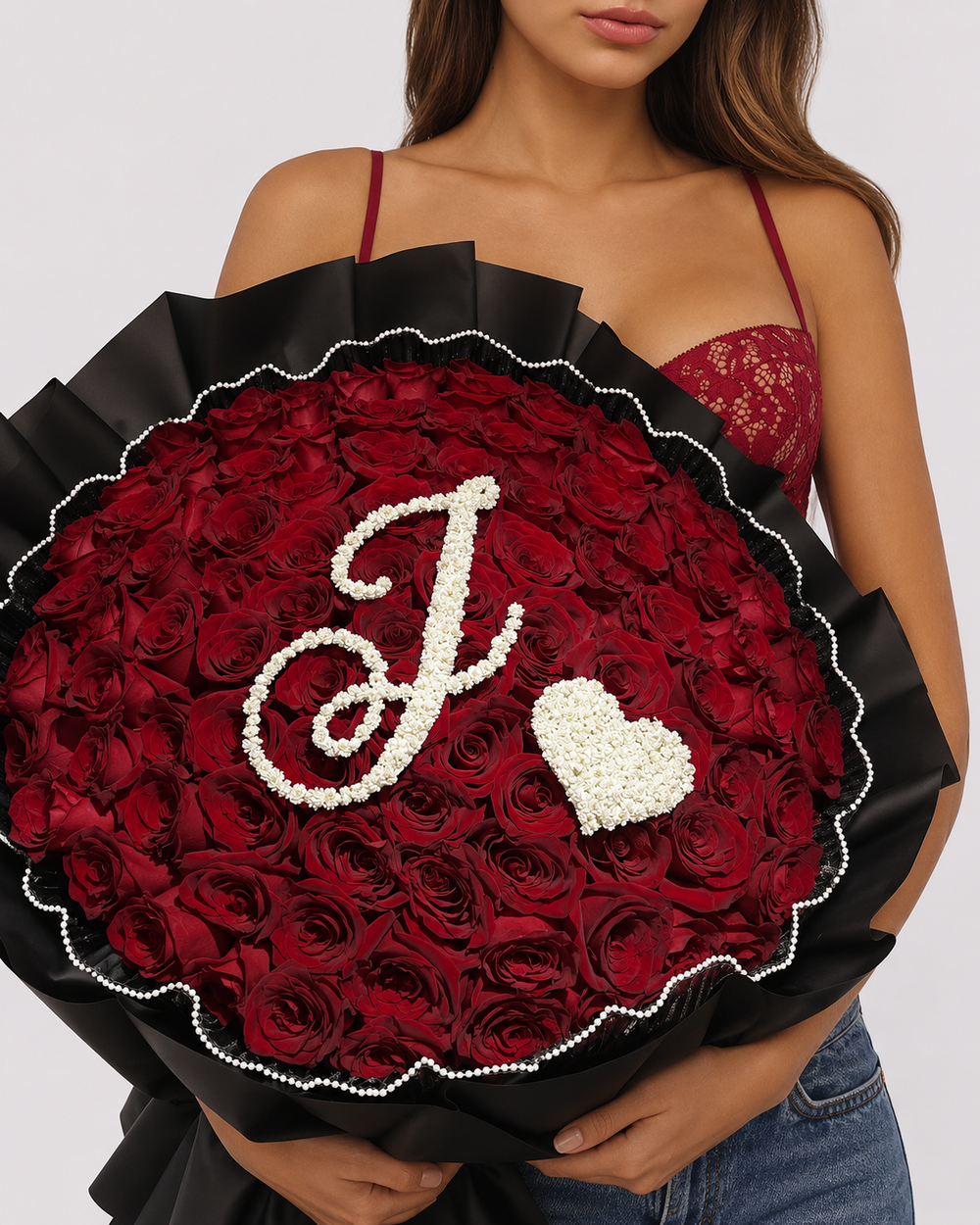 Bouquet Ava de roses rouges fraîches porté par une femme, papier noir, lettre J et cœur en gypsophile