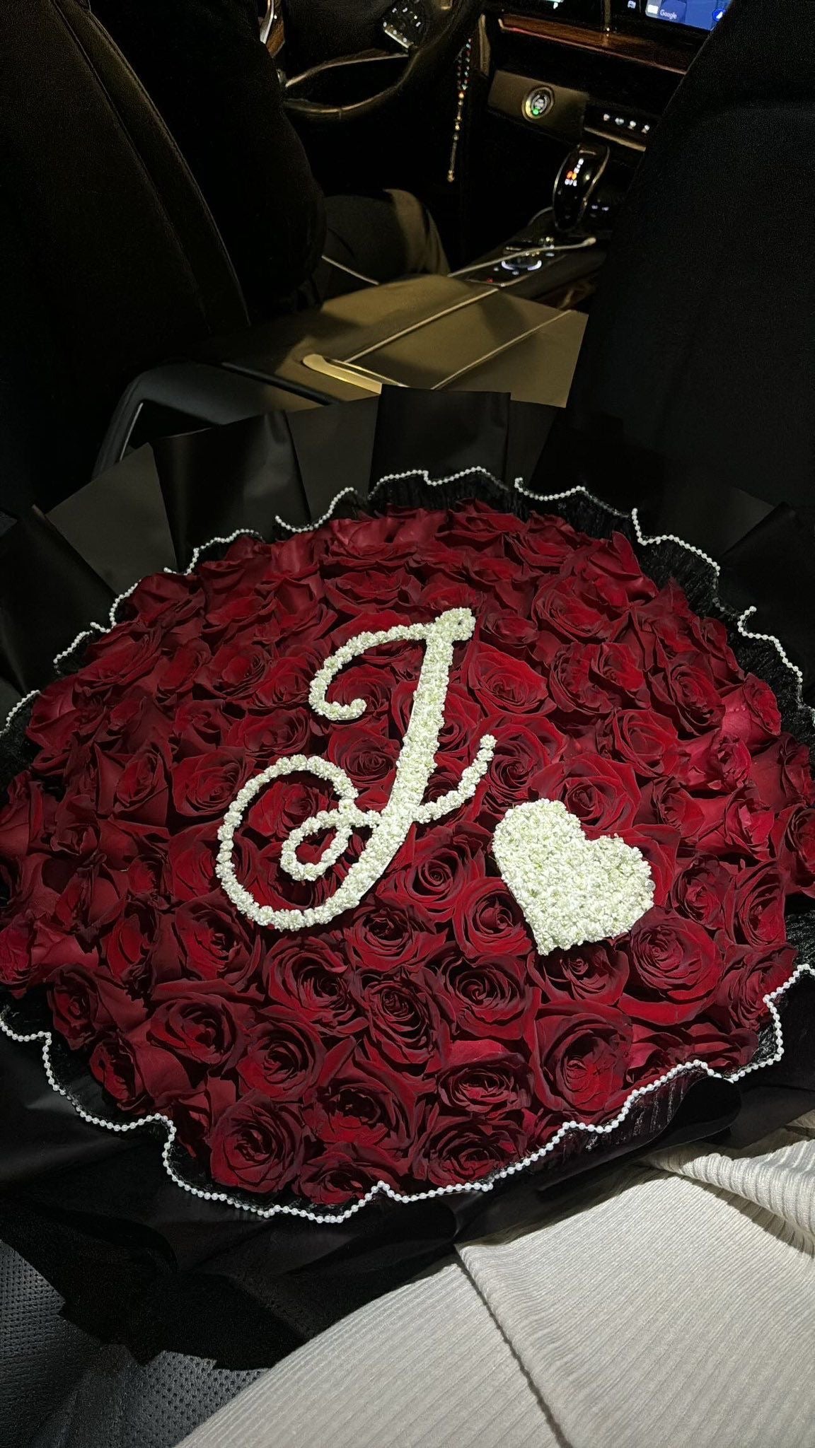 Bouquet Ava de roses rouges fraîches avec lettre J et cœur en gypsophile, vu de nuit dans une voiture