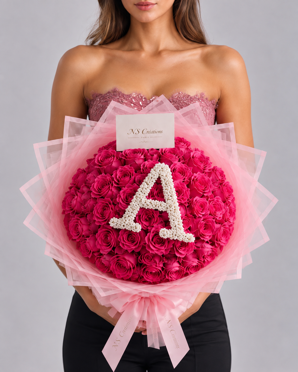 Bouquet Bella de roses roses fraîches porté par une femme, avec lettre A en gypsophile et emballage tulle rose