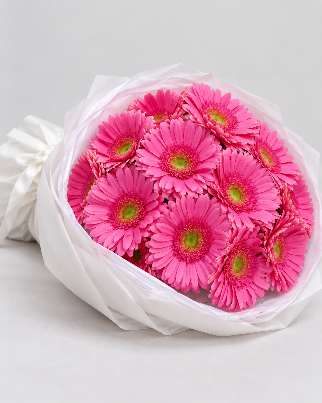 Bouquet Alinea de gerberas roses posé de côté, papier blanc et ruban blanc