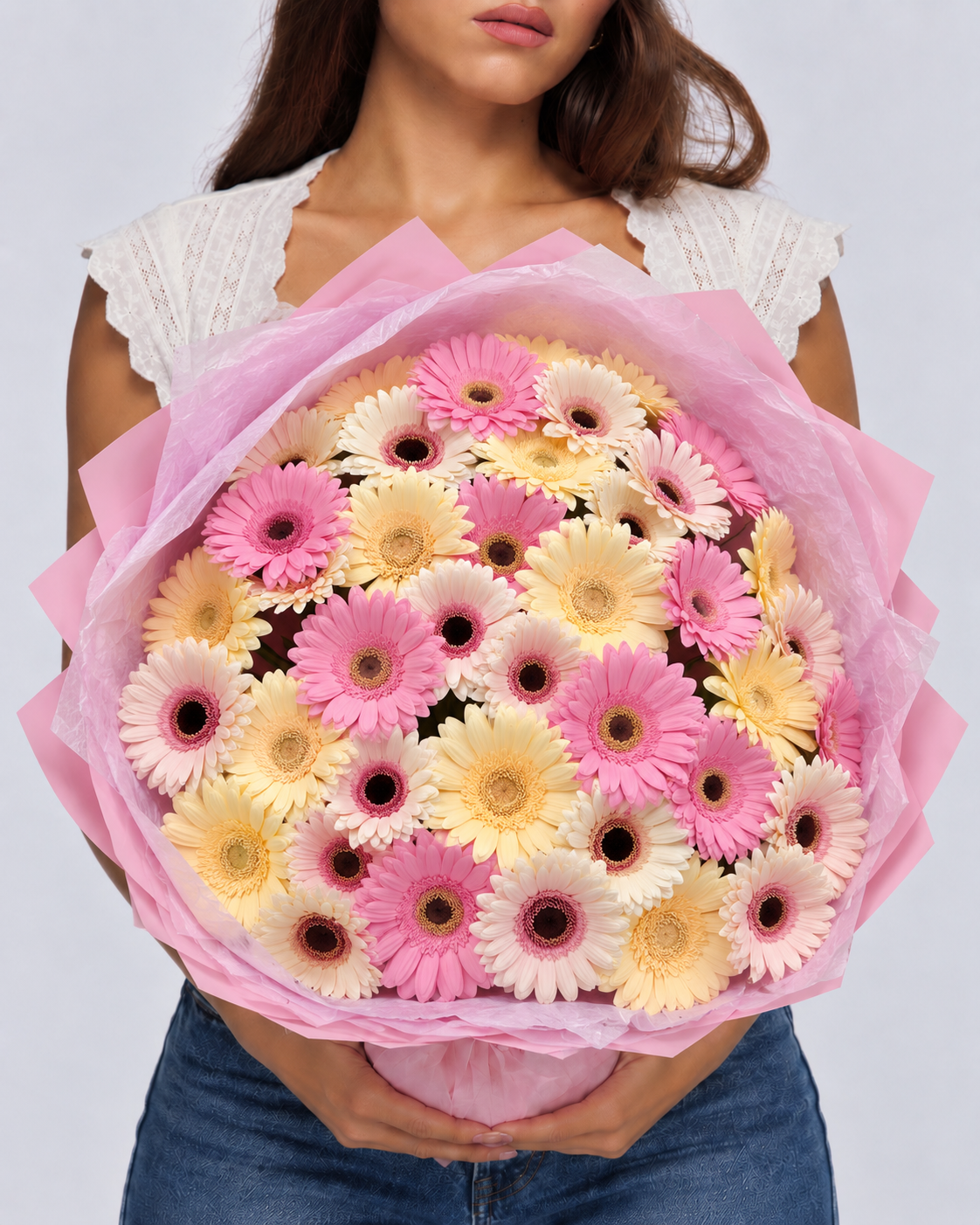 Bouquet Cosette de gerberas frais roses et jaunes en papier rose, tenu devant soi