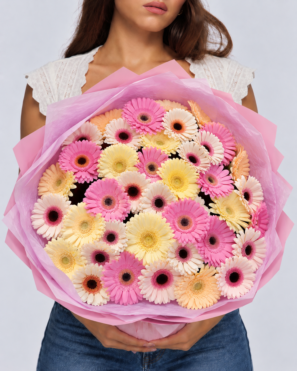Bouquet Cosette de gerberas roses, jaunes et crème tenu à deux mains