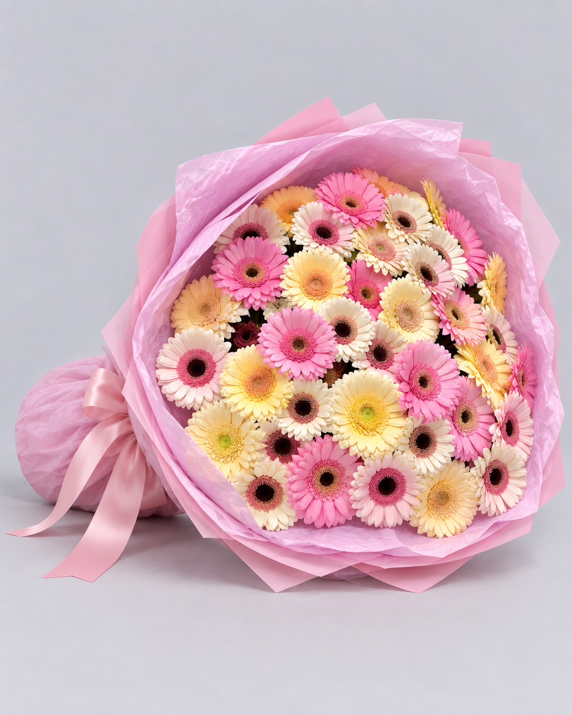Bouquet Cosette de gerberas posé de côté, papier rose plissé et ruban rose