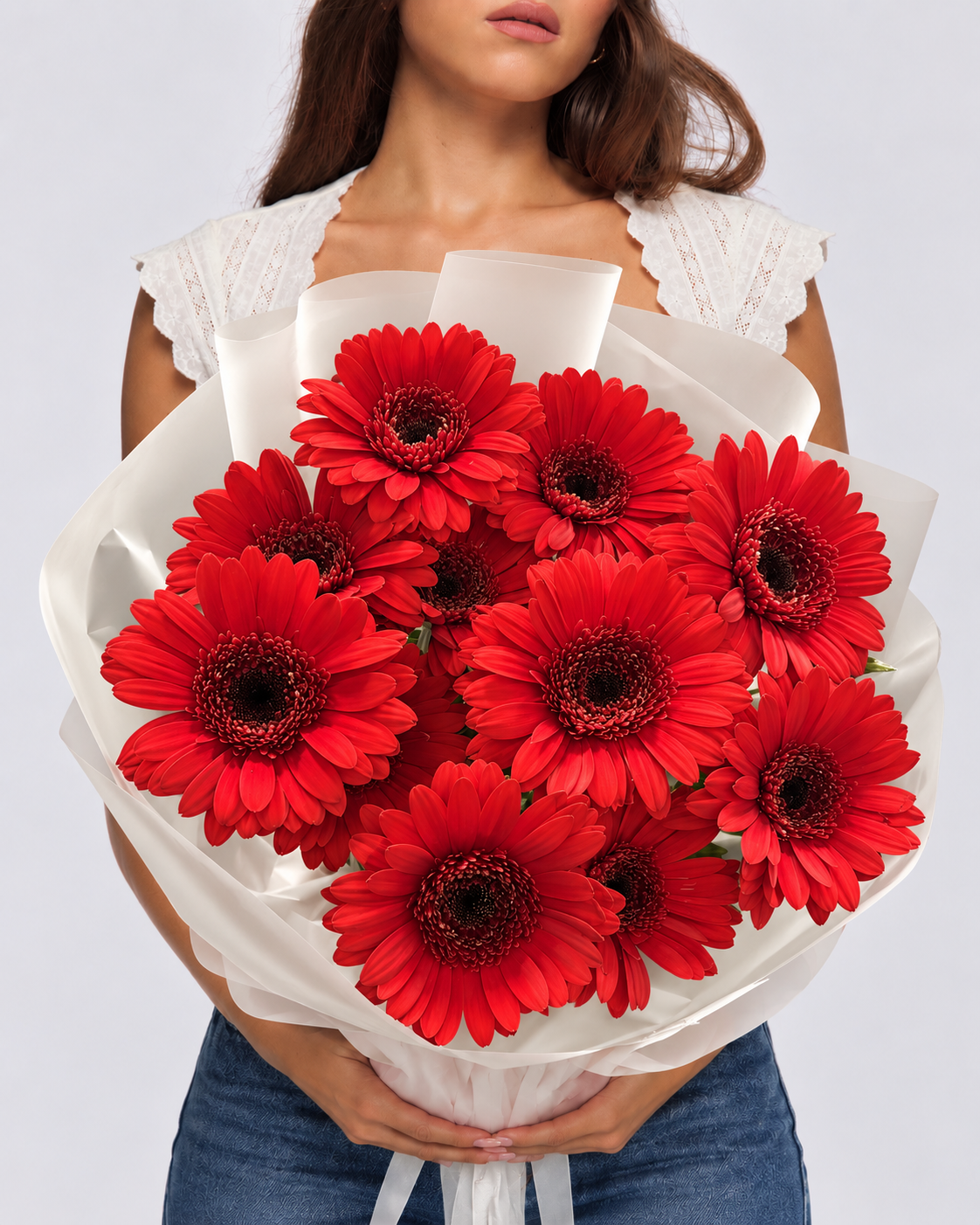 Bouquet Iman de gerberas rouges tenu à deux mains, papier blanc translucide