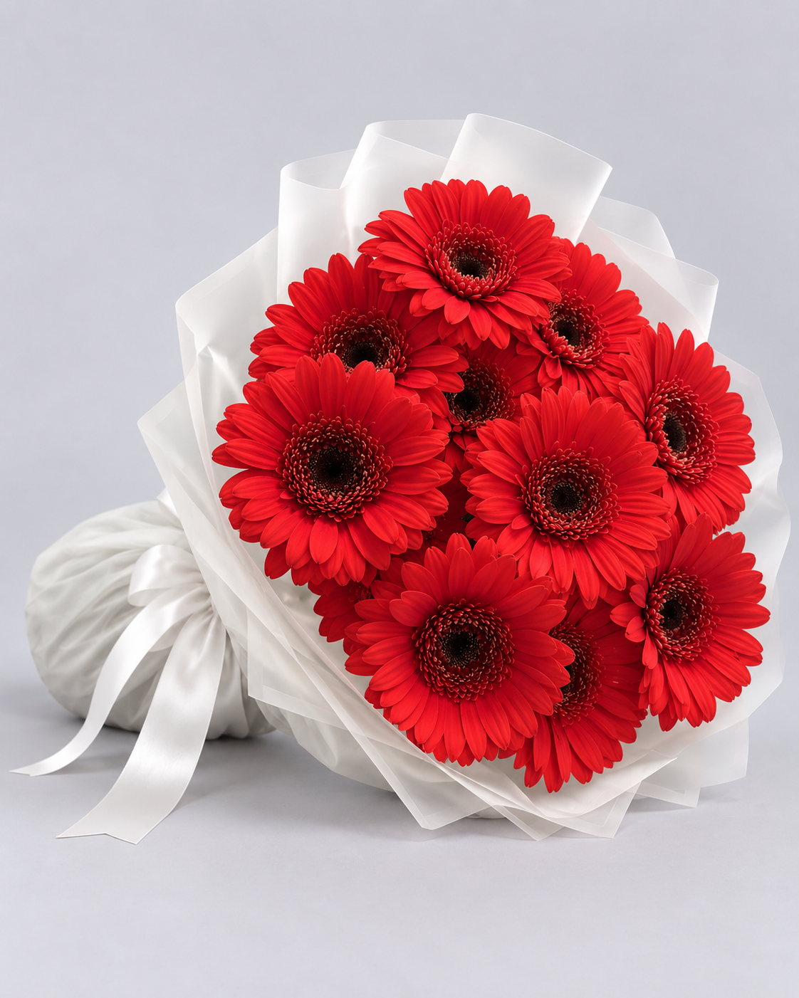 Bouquet Iman de gerberas rouges posé de côté, papier blanc et ruban blanc
