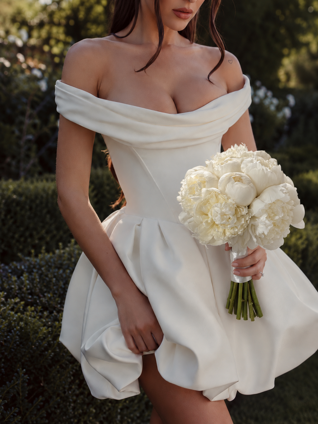 Femme en robe blanche à épaules dénudées tenant le bouquet de mariée Alba, pivoines blanches