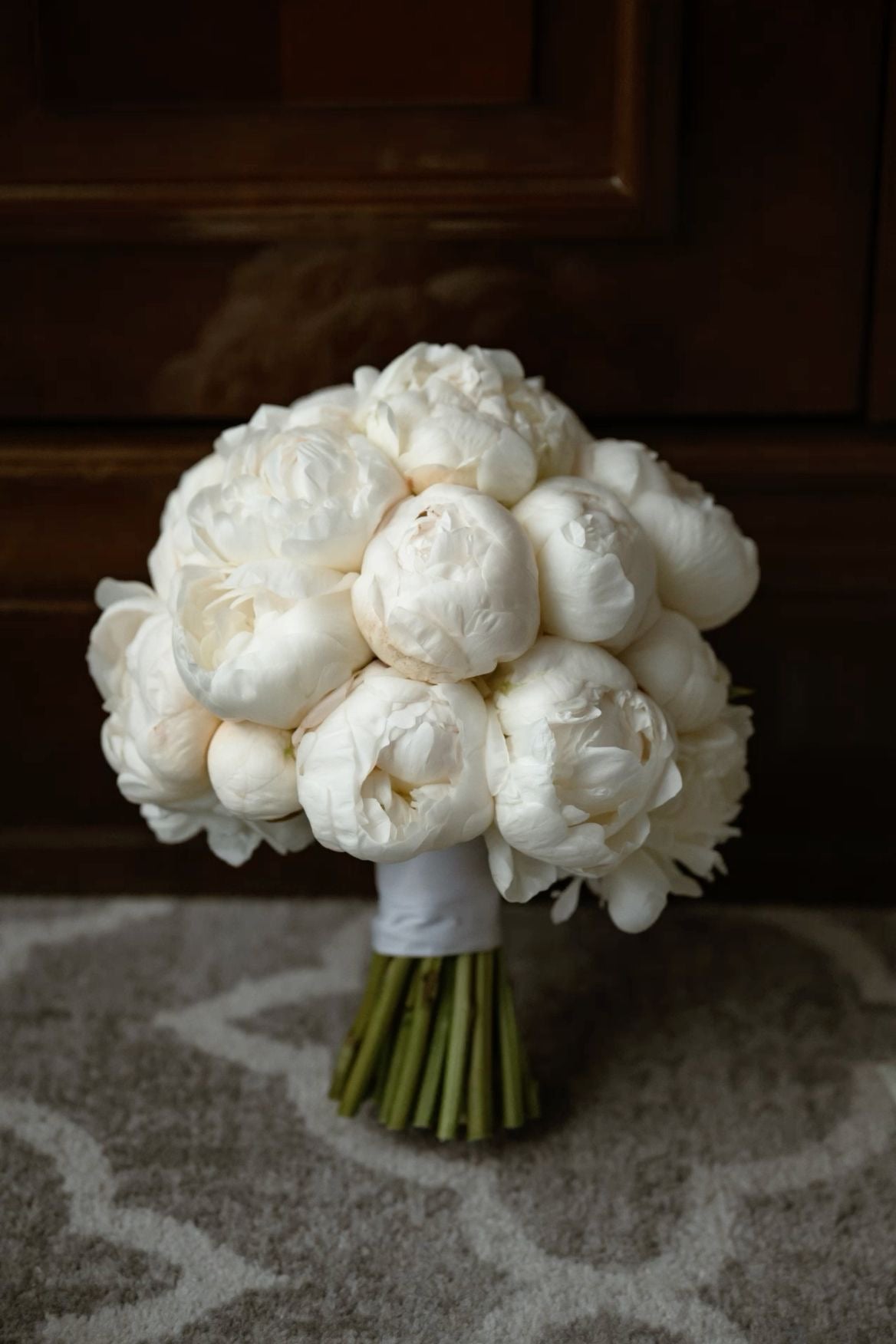 Bouquet de mariée Alba de pivoines blanches posé sur un tapis, fond sombre