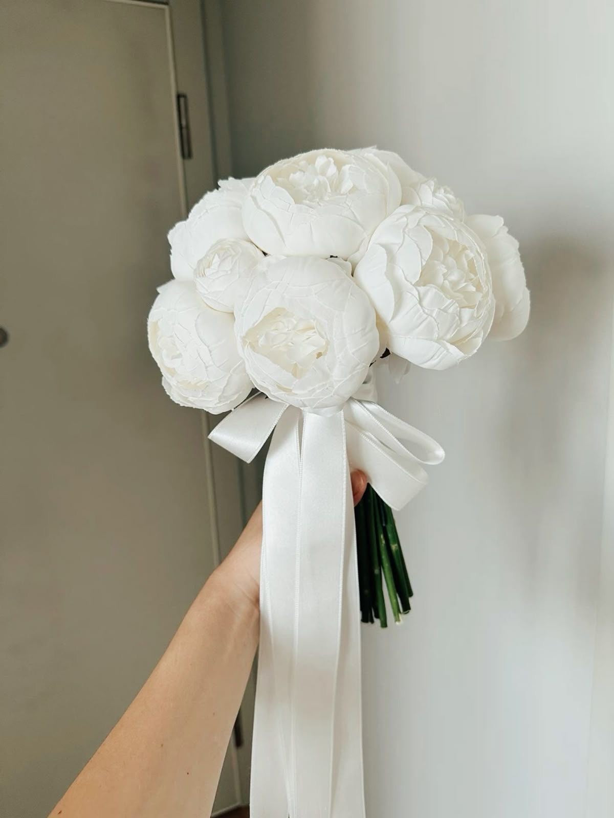 Bouquet de mariée Alba de pivoines blanches tenu en main avec long ruban blanc