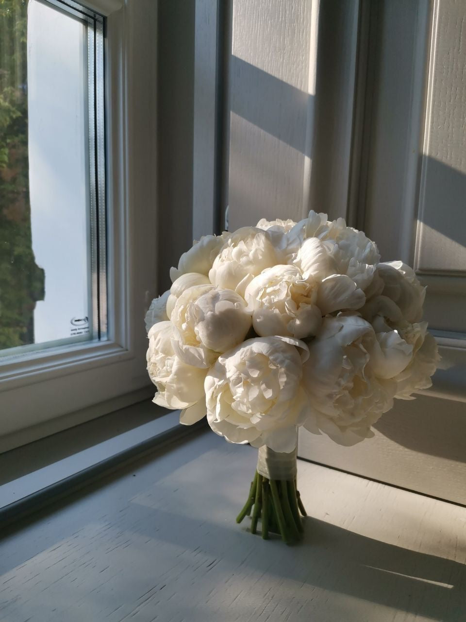 Bouquet de mariée Alba de pivoines blanches posé près d'une fenêtre