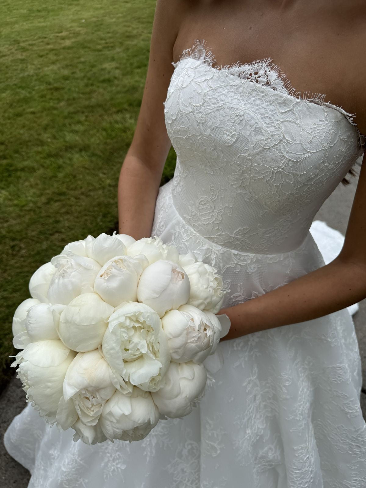Mariée en robe bustier tenant le bouquet de mariée Alba de pivoines blanches en extérieur