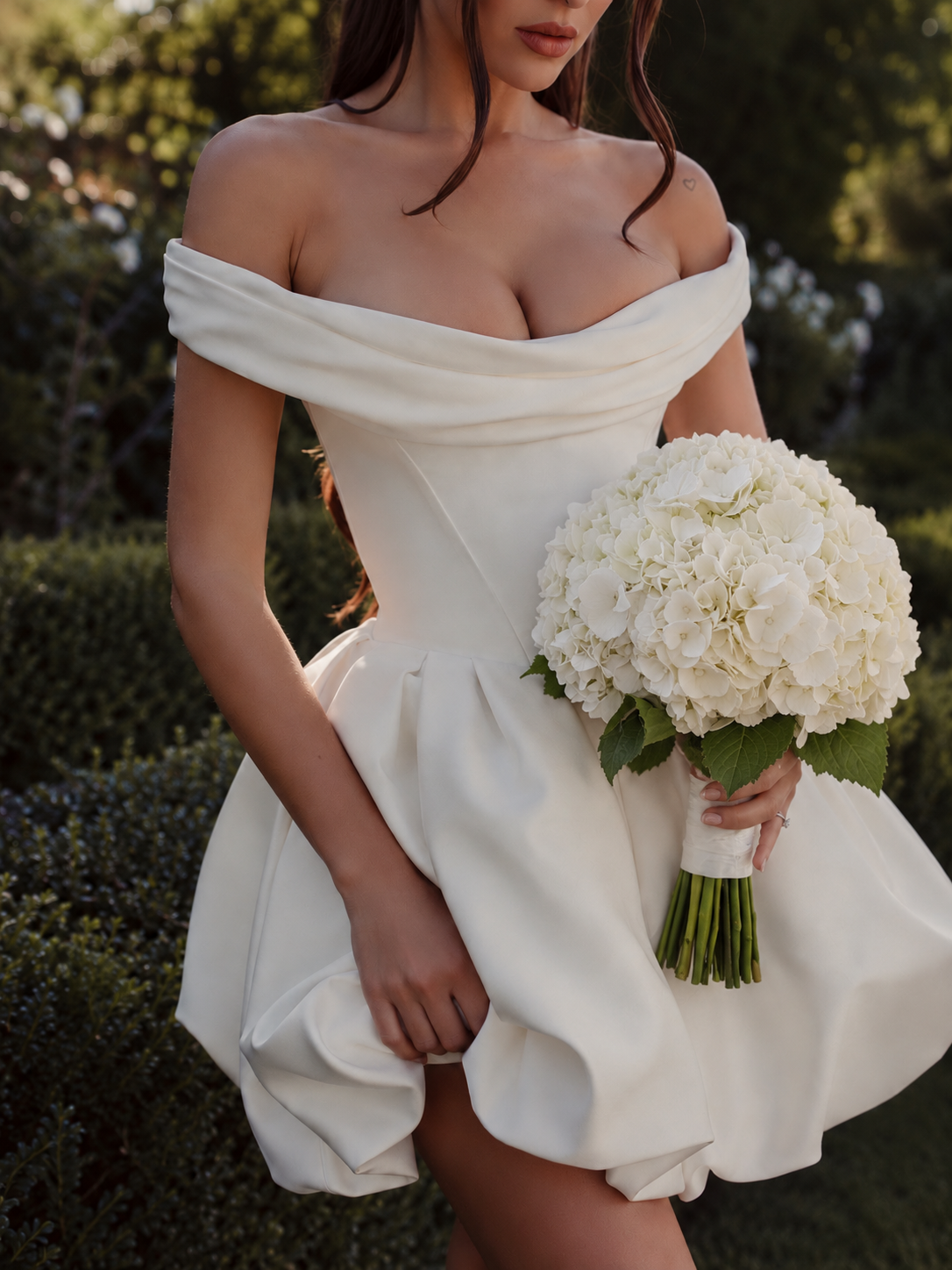 Femme en robe blanche à épaules dénudées tenant le bouquet de mariée Alexandra, hortensias blancs