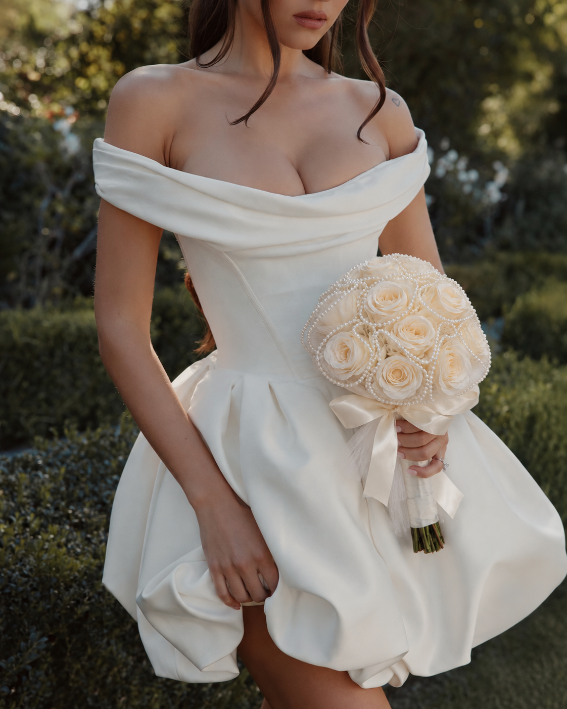 Mariée en robe blanche courte tenant le bouquet de mariée Divas, roses crème et perles