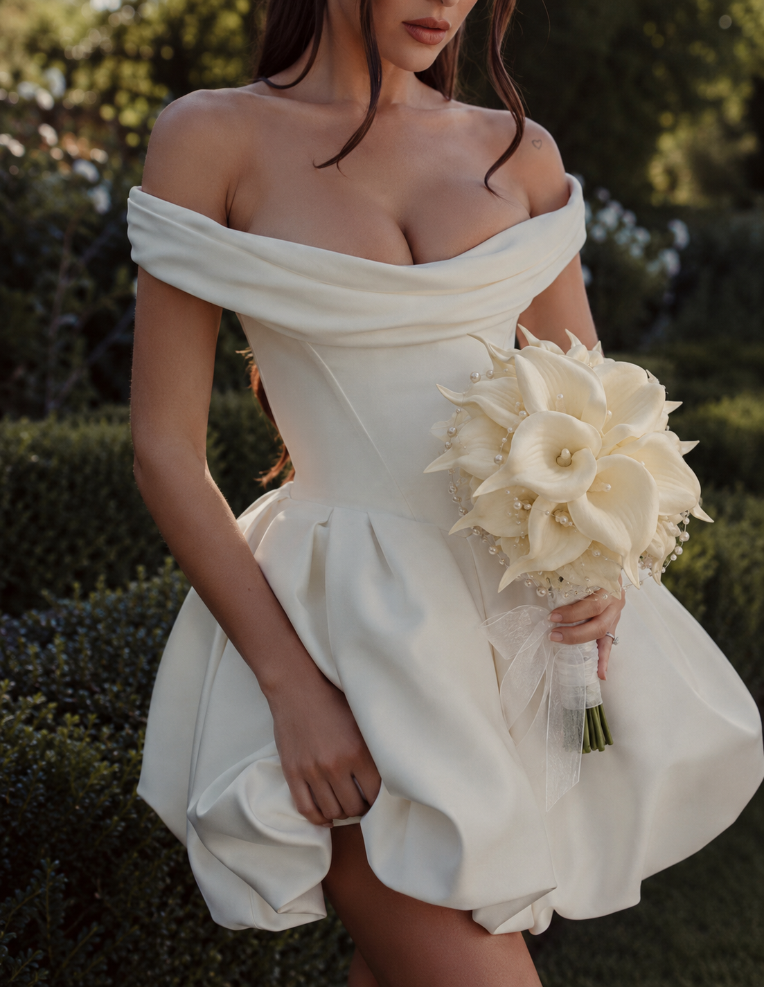 Mariée en robe blanche courte tenant le bouquet de mariée Leonore, arums crème