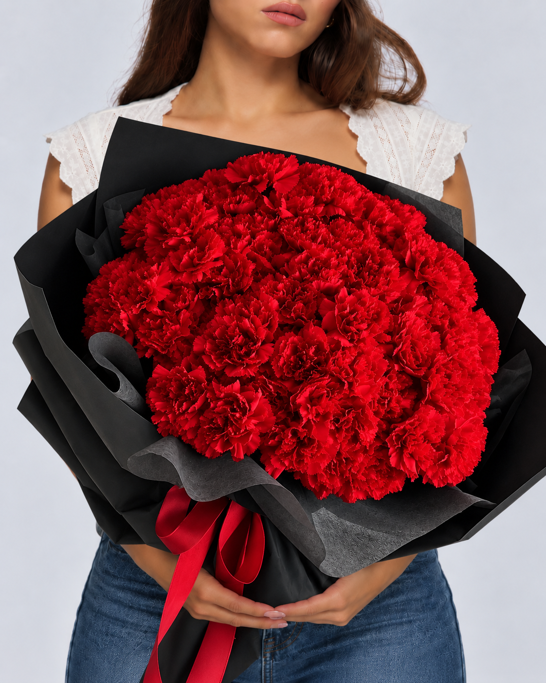 Bouquet Mimi d'œillets rouges tenu à deux mains, papier noir plissé et ruban rouge