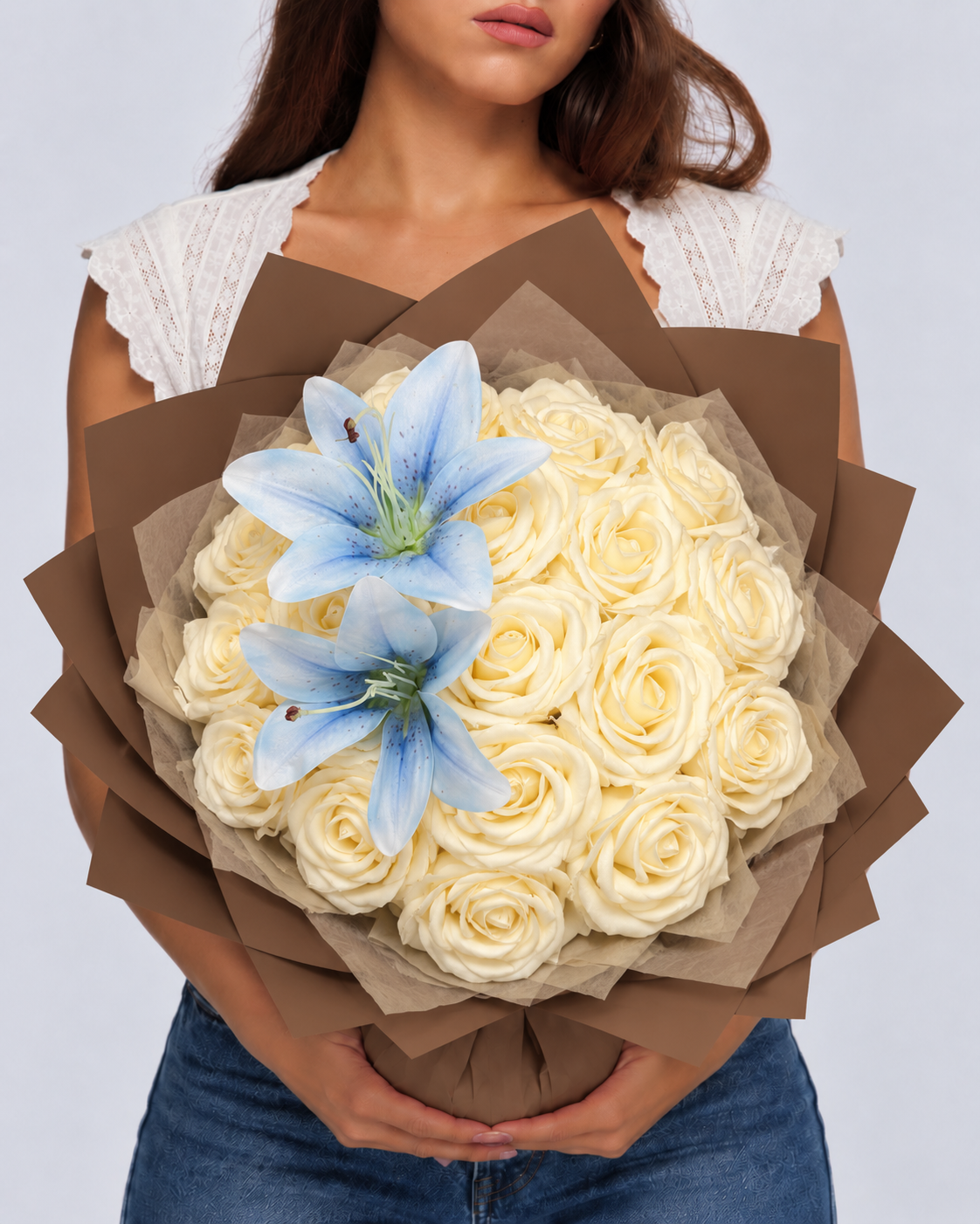 Bouquet Vaea de roses éternelles vanille et deux lys bleu ciel tenu devant soi, papier kraft marron