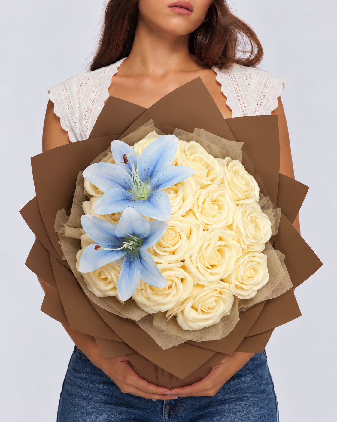 Bouquet Vaea tenu à deux mains, roses vanille crème, lys bleu ciel et papier kraft marron