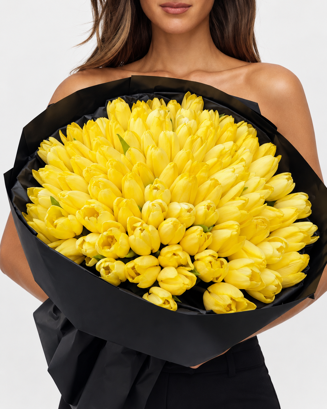 Bouquet Zoe de tulipes jaunes tenu à deux mains, papier noir plissé