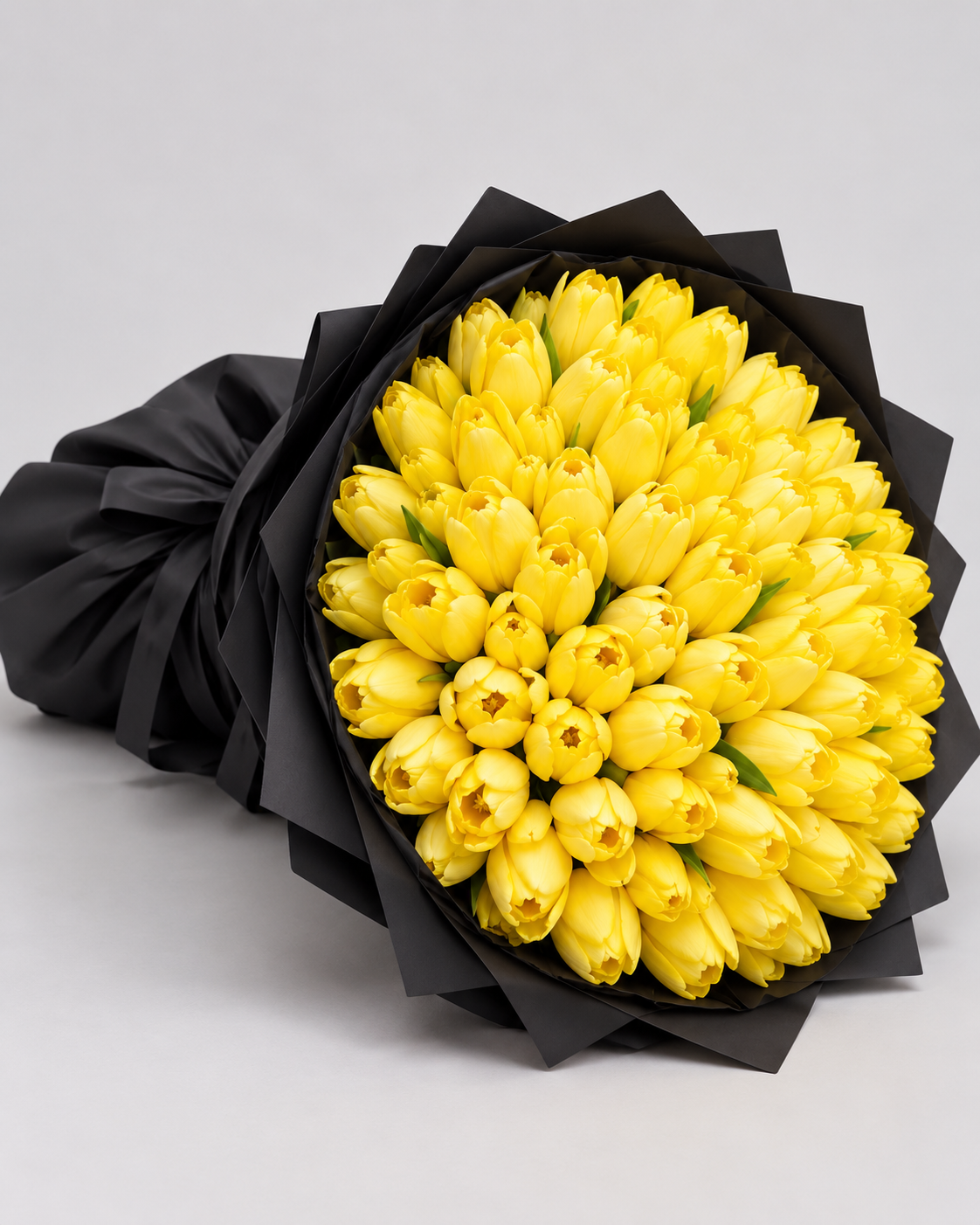 Bouquet Zoe de tulipes jaunes posé de côté, papier noir et nœud noir