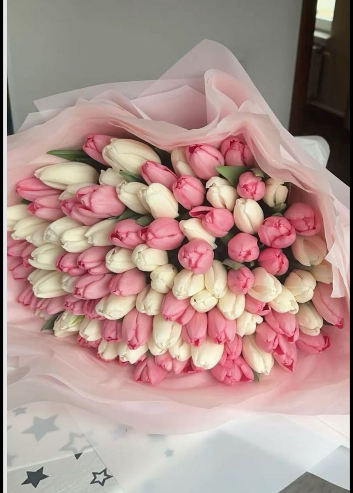 Bouquet Cadie de tulipes roses et blanches dans un papier rose pâle, posé sur une table