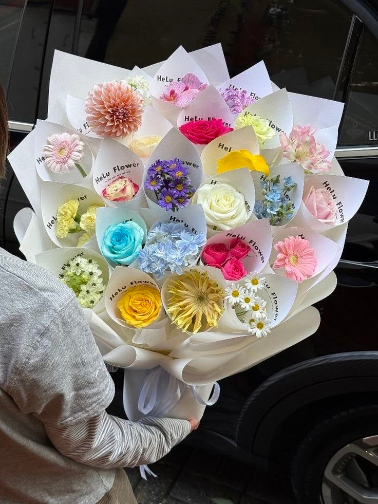 Bouquet CAPRICE de fleurs fraîches multicolores en emballage blanc, tenu à la main, photo réelle