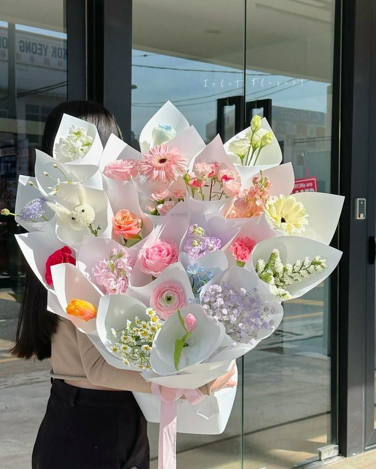 Bouquet CAPRICE de fleurs fraîches multicolores aux teintes pastel porté à l'extérieur, photo réelle