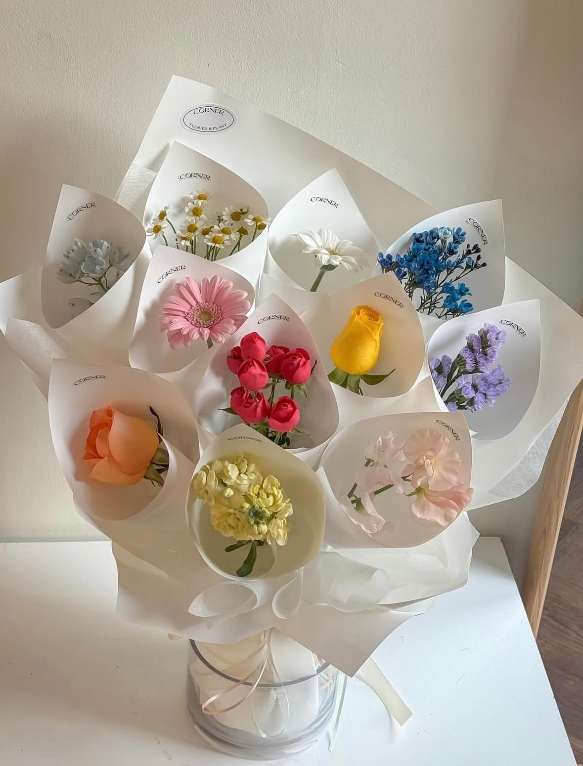 Bouquet CAPRICE de fleurs fraîches multicolores en papier blanc posé sur une table, photo réelle