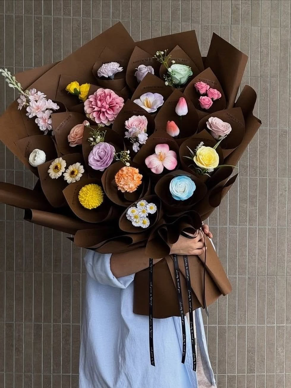 Bouquet CAPRICE de fleurs fraîches multicolores en emballage kraft marron, tenu à la main