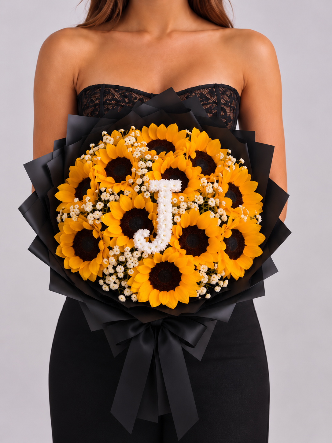 Bouquet Chloé de tournesols et gypsophile avec lettre J, papier noir, porté par une femme