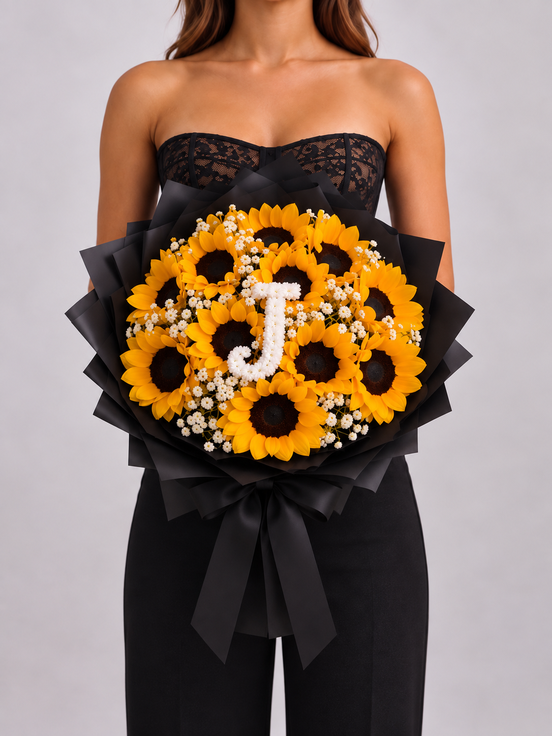Bouquet Chloé de tournesols avec lettre J tenu dans les bras, ruban noir, vue de face
