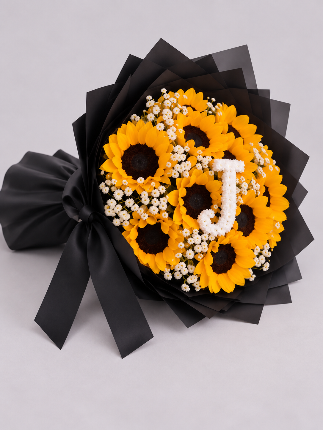 Bouquet Chloé de tournesols et gypsophile avec lettre J posé sur fond clair, vue de côté
