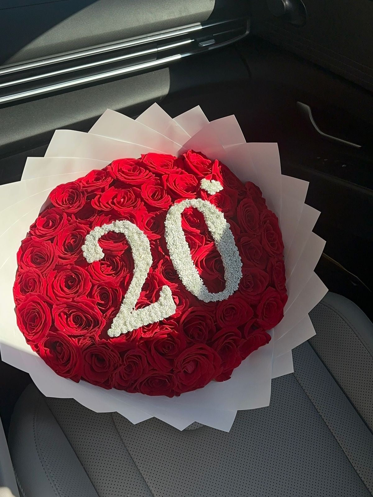 Bouquet Demi de roses rouges avec chiffre 20 posé sur un siège de voiture
