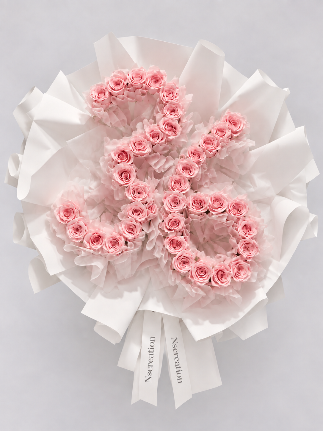 Bouquet Elana de roses roses en forme de chiffre posé sur fond clair, ruban blanc