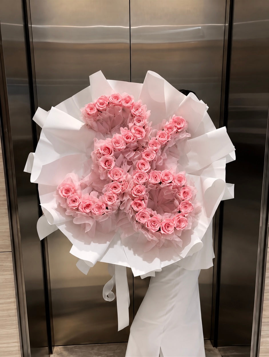 Bouquet Elana de roses roses en forme de chiffre tenu devant un ascenseur, papier blanc