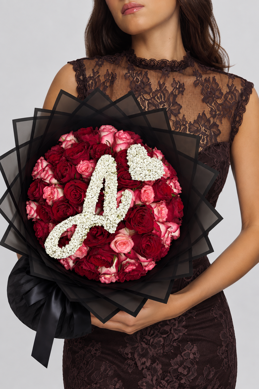 Bouquet Esme de roses rouges et roses fraîches porté par une femme, papier noir, lettre A et cœur en gypsophile