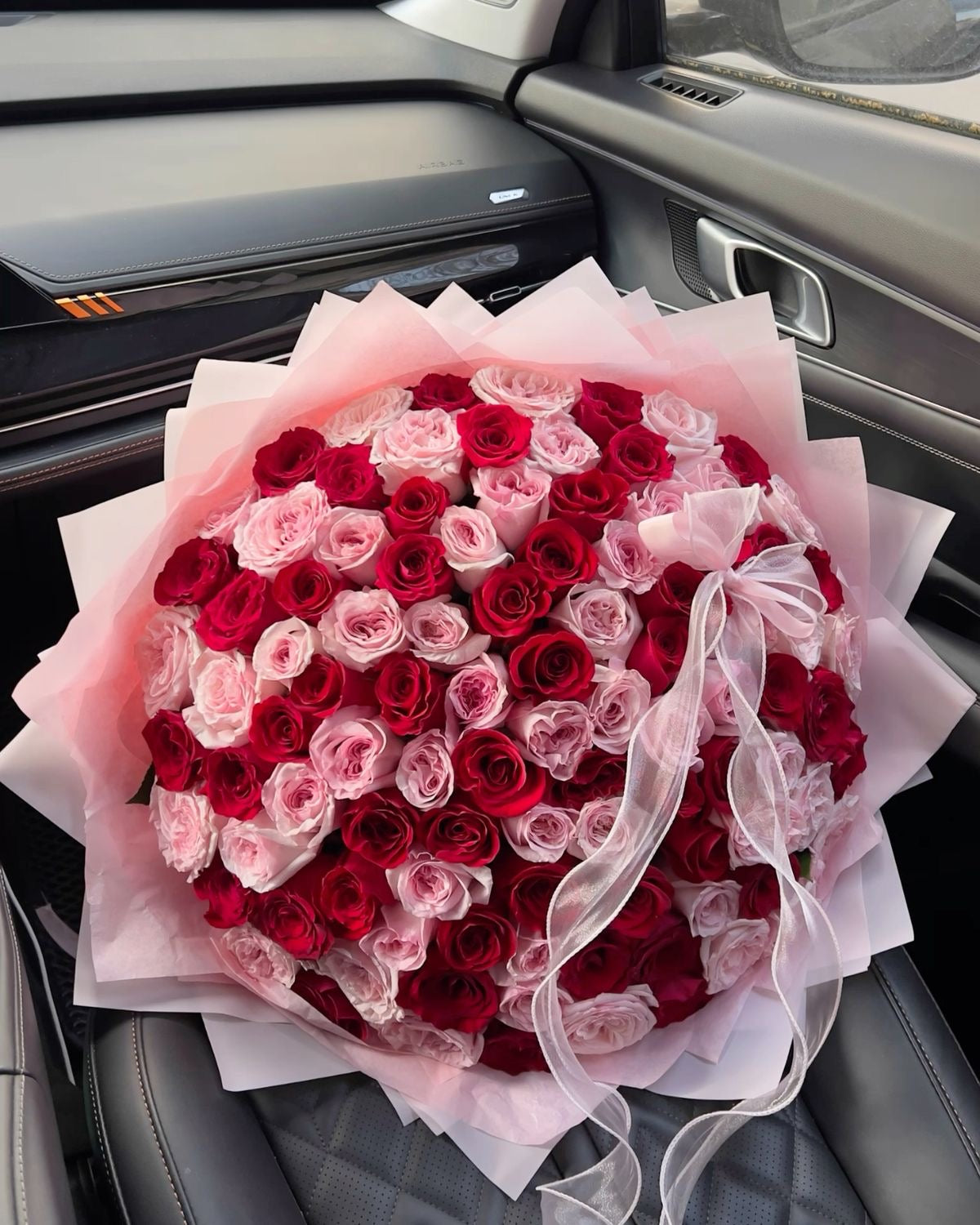 Grand bouquet Esme de roses rouges et roses fraîches, papier rose pâle et ruban, dans une voiture