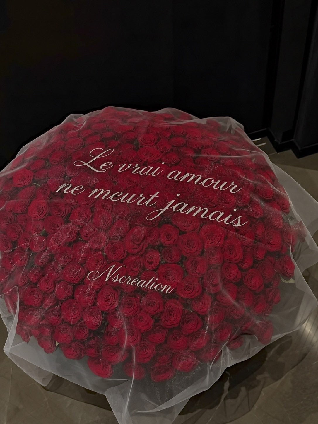 Bouquet JANNA de roses rouges fraîches sous tulle avec la phrase Le vrai amour ne meurt jamais, photo réelle