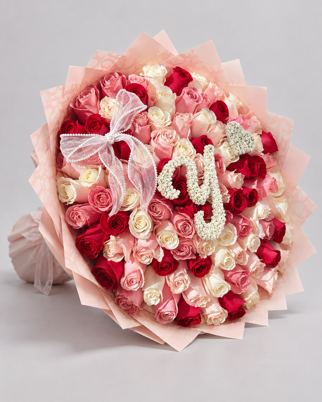 Bouquet Juliette de roses avec lettre et nœud rose posé sur fond clair, vue de côté