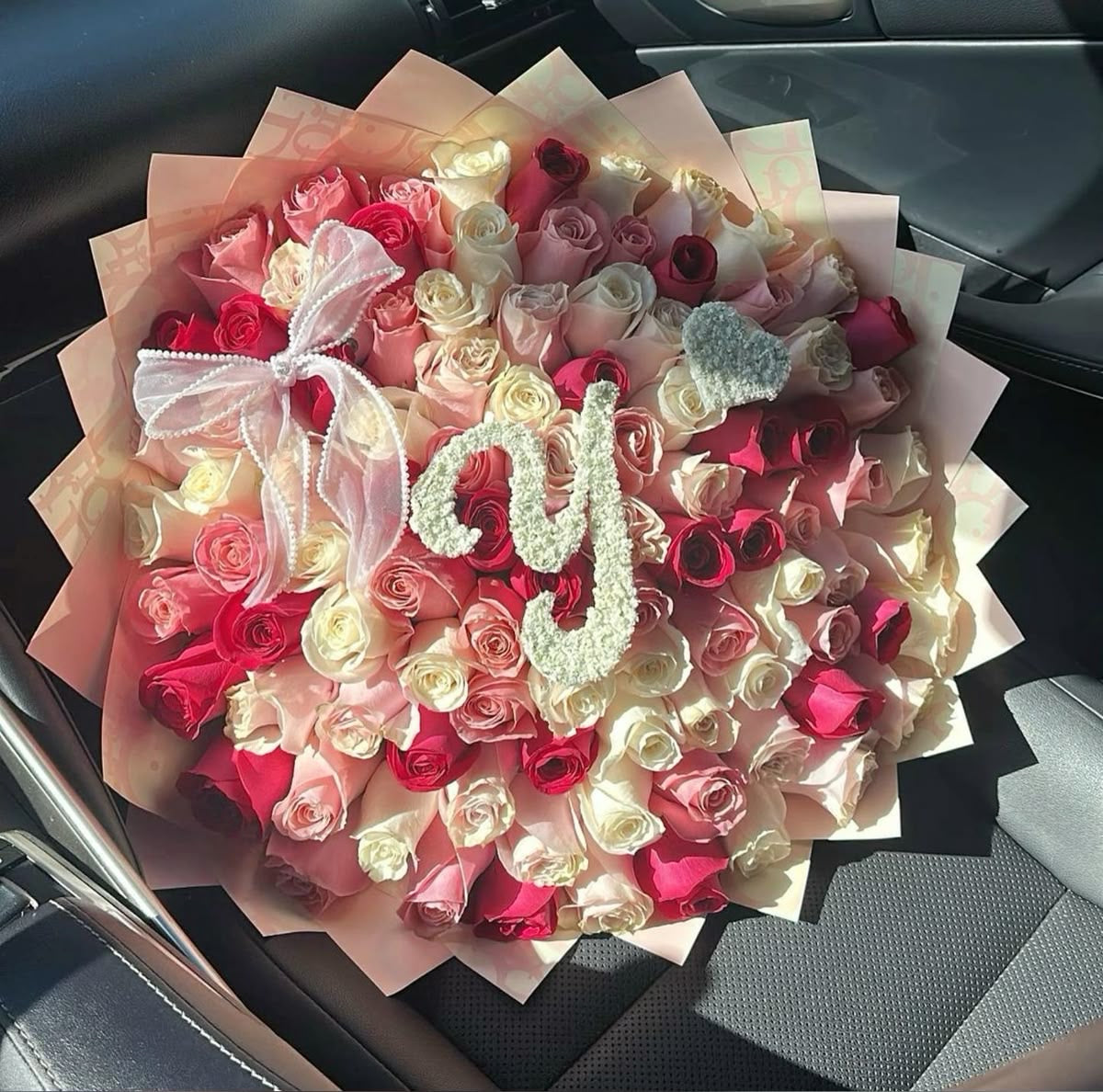 Bouquet Juliette de roses avec lettre décorative posé sur un siège de voiture