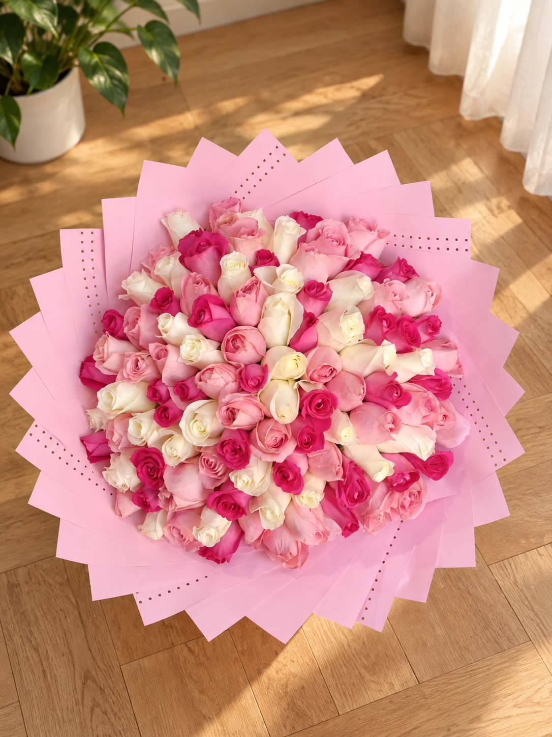 Bouquet Juliette de roses rouges, roses et blanches posé sur un parquet, papier rose