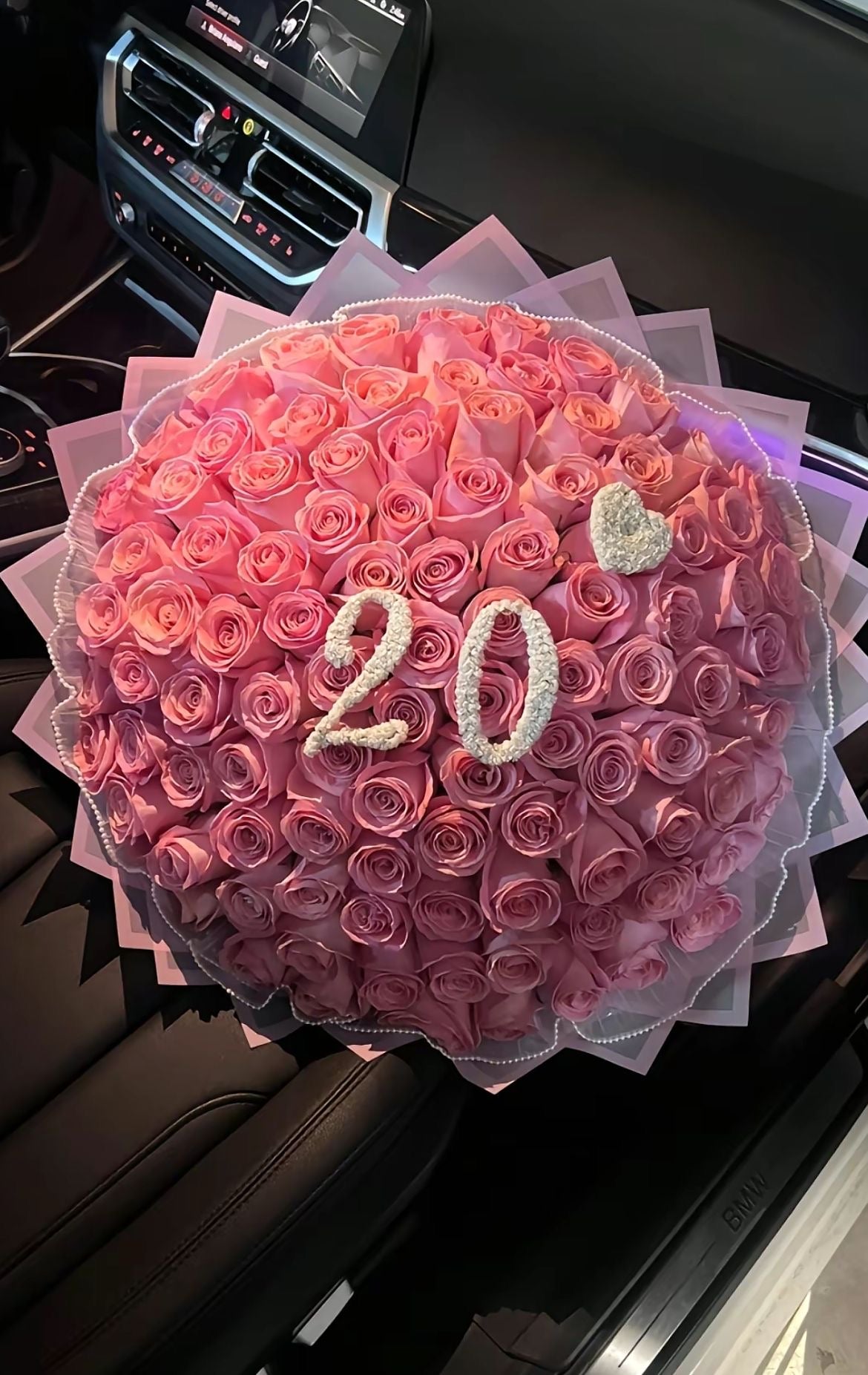 Bouquet Kikky de roses roses avec chiffre 20 posé sur un siège de voiture