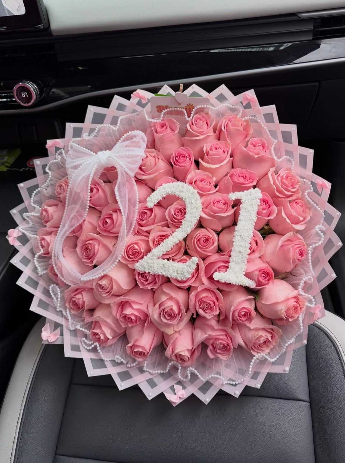 Bouquet Kikky de roses roses avec chiffre 21 et nœud blanc sur un siège de voiture