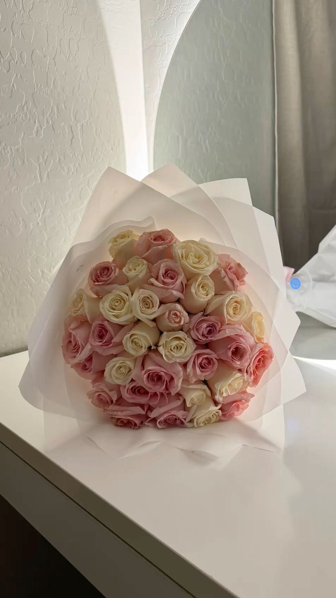 Bouquet Mademoiselle moyen de roses blanches et roses fraîches, papier blanc, posé sur un meuble