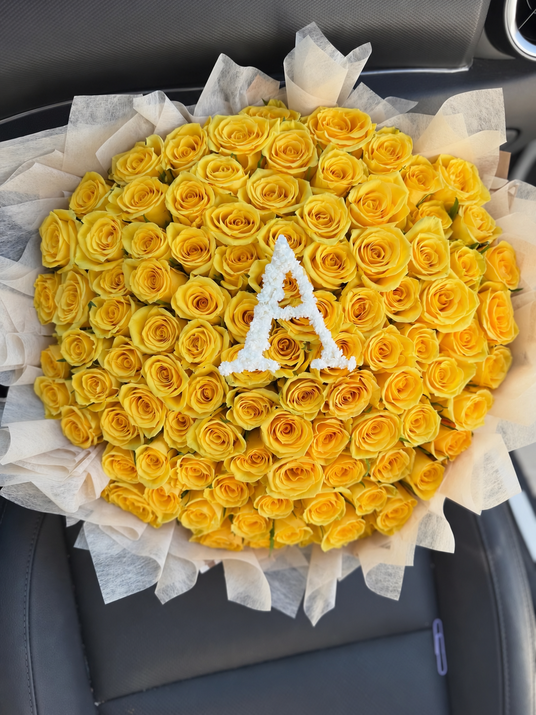 Bouquet Mia de roses jaunes avec lettre A posé sur un siège de voiture