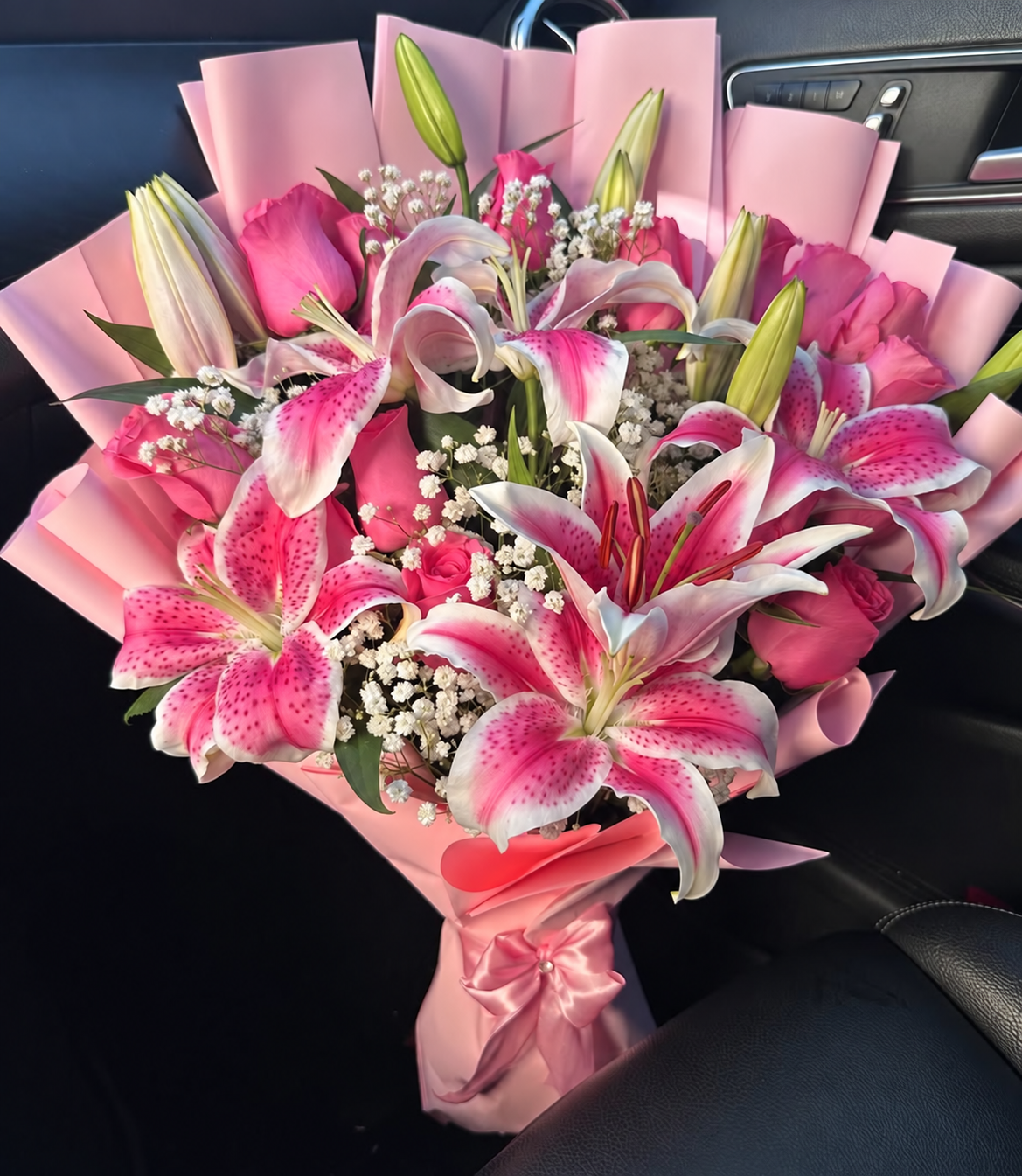 Bouquet Muse de lys roses et roses posé sur un siège de voiture
