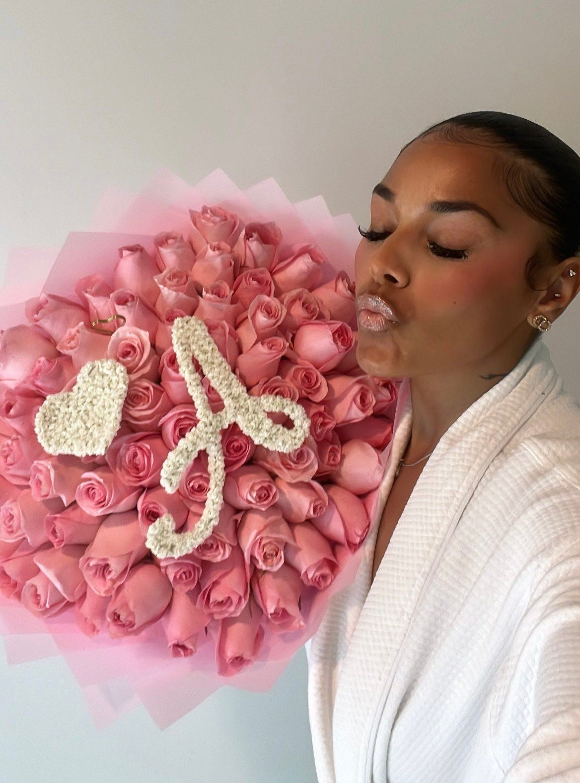 Cliente avec un bouquet Penelope de roses roses fraîches orné d'une lettre et d'un cœur en gypsophile