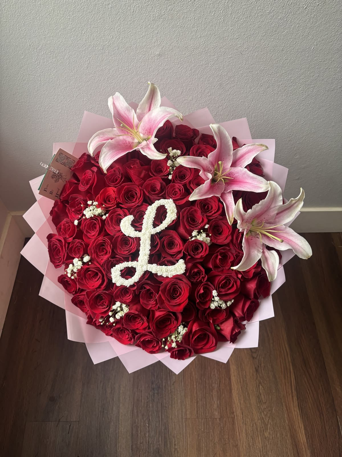 Bouquet Selma de roses rouges et lys roses avec une initiale décorative, posé à plat